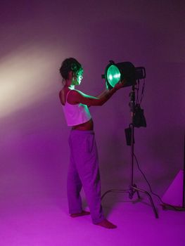 A woman in casual attire adjusts vibrant studio lighting in an artistic setup.
