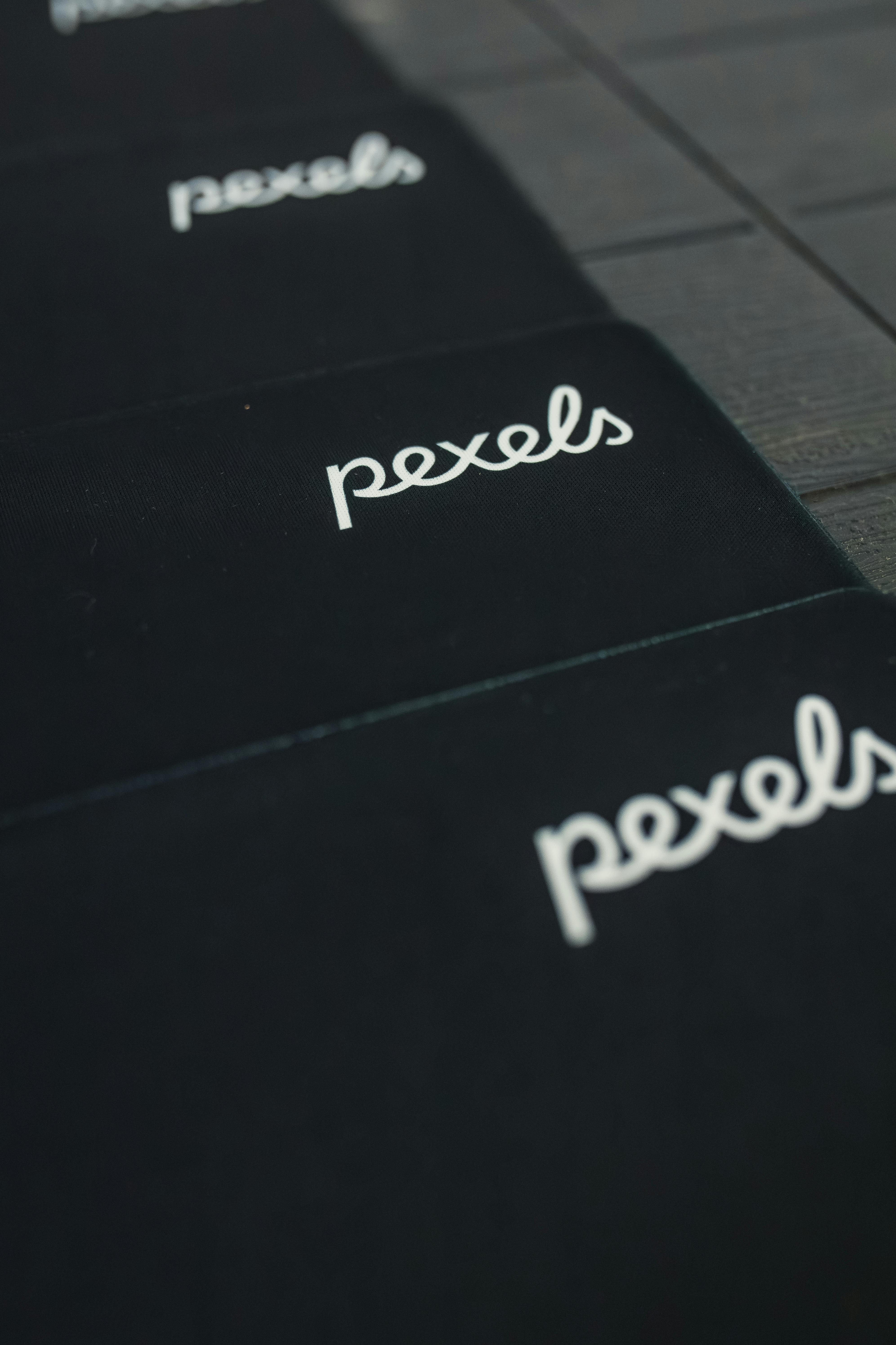 免费 Pexels 徽标的特写视图，以重复的图案显示在深色表面上。 素材图片