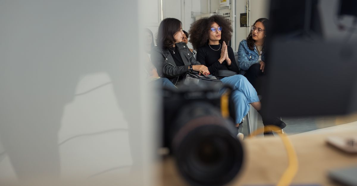 Three adults engaged in a casual conversation in an indoor setting, captured candidly.