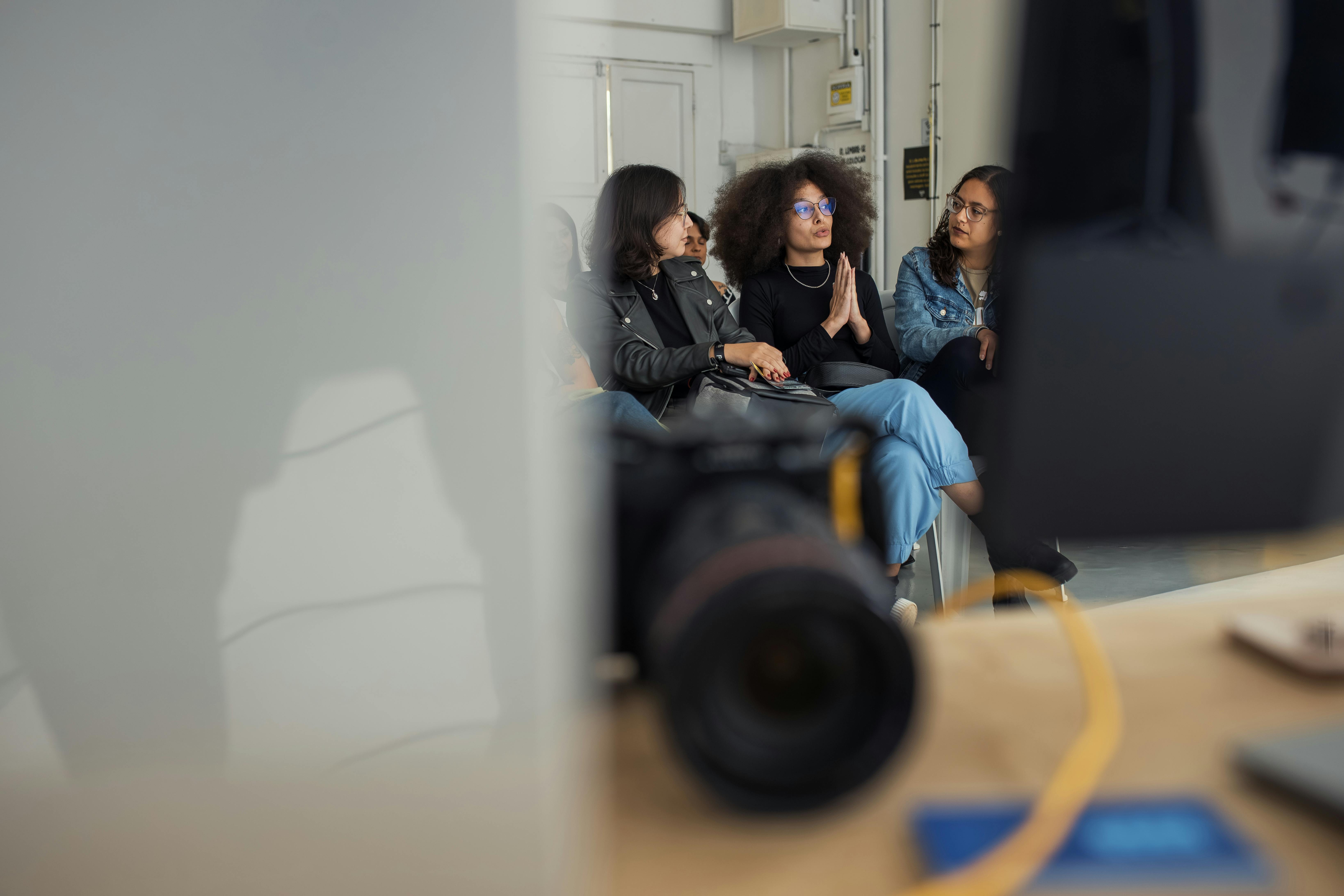 grátis Três adultos envolvidos em uma conversa casual em um ambiente interno, capturados com franqueza. Foto profissional