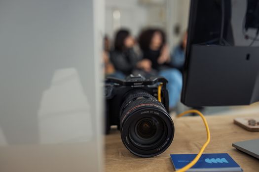 Front view of a DSLR camera on a desk with a blurred group of adults in discussion behind it.