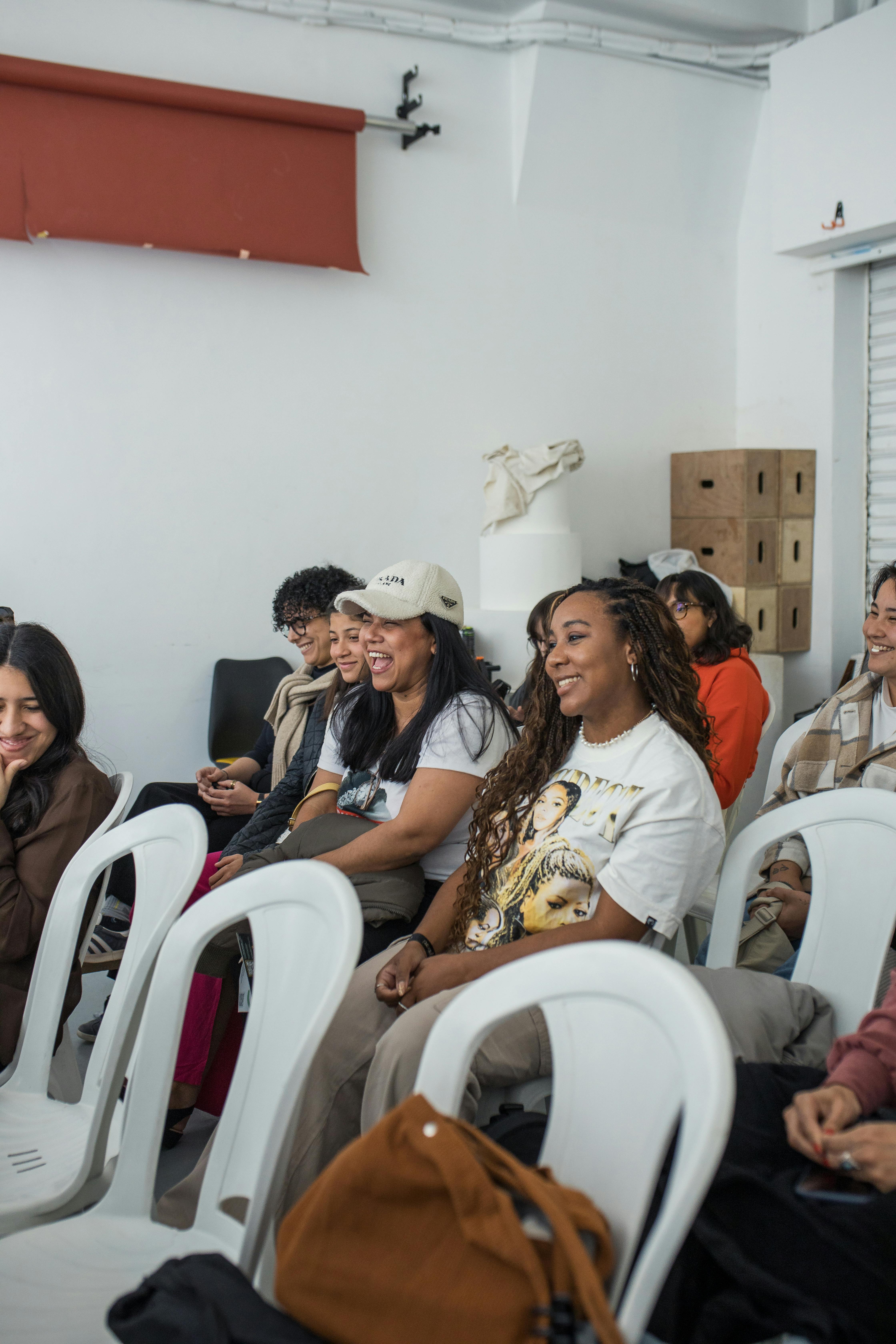 A group of diverse adults attentively listening during an indoor seminar, seated on white chairs.