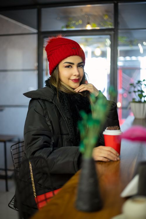 Free Stylish woman in a café enjoying hot coffee, dressed warmly in a red beanie and black jacket. Stock Photo