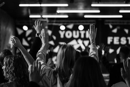 Black and white photo of an enthusiastic crowd at a youth festival, raising hands.
