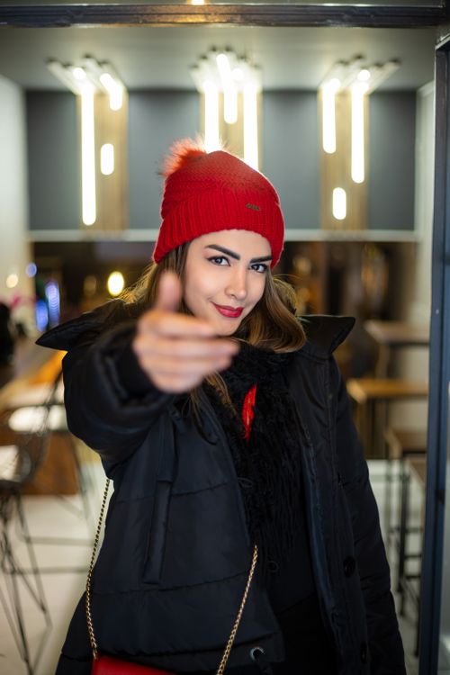 Free Stylish woman in red beanie posing confidently in a modern cafe setting. Stock Photo