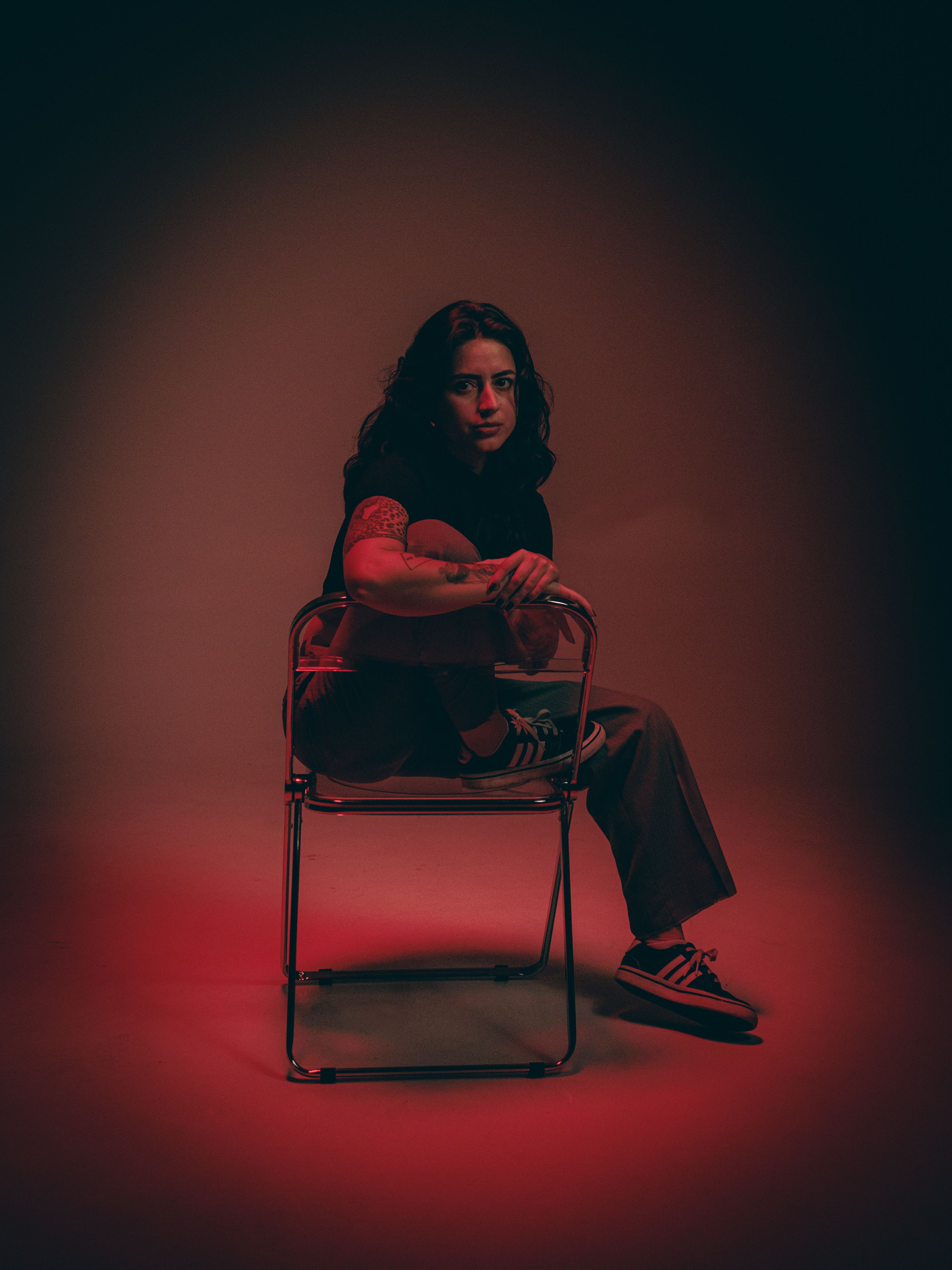 Moody portrait of a young adult seated under red lighting, creating a dramatic atmosphere.