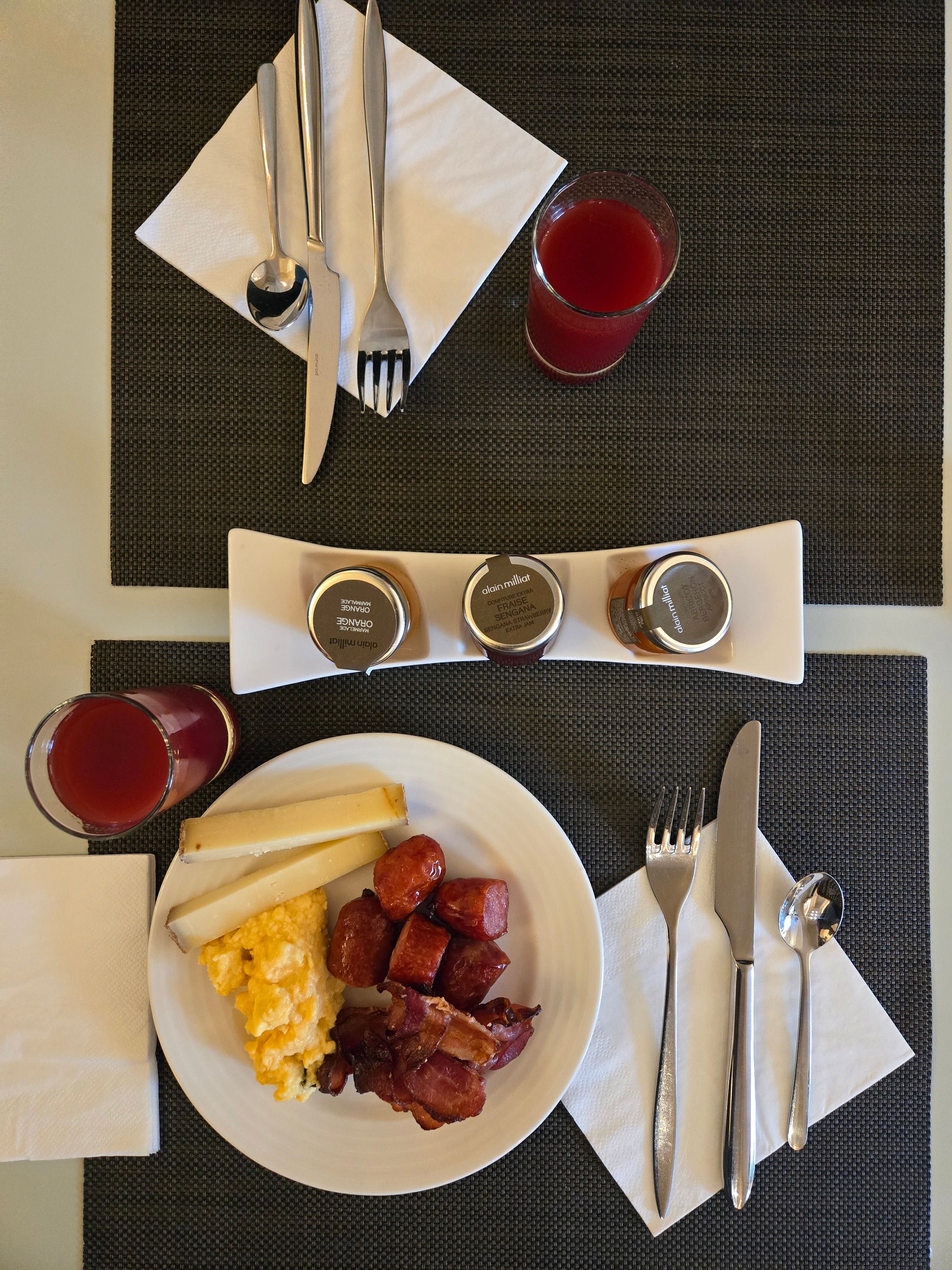 Scrambled eggs, bacon, and sausages with juice on a dining table.