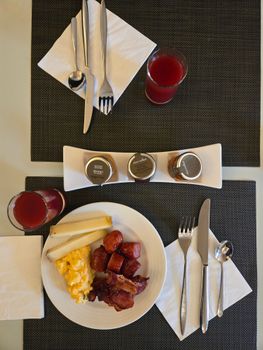 Scrambled eggs, bacon, and sausages with juice on a dining table.