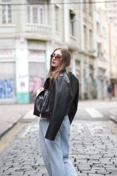 Stylish woman in sunglasses and leather jacket posing on a cobblestone street in Curitiba, Brazil.
