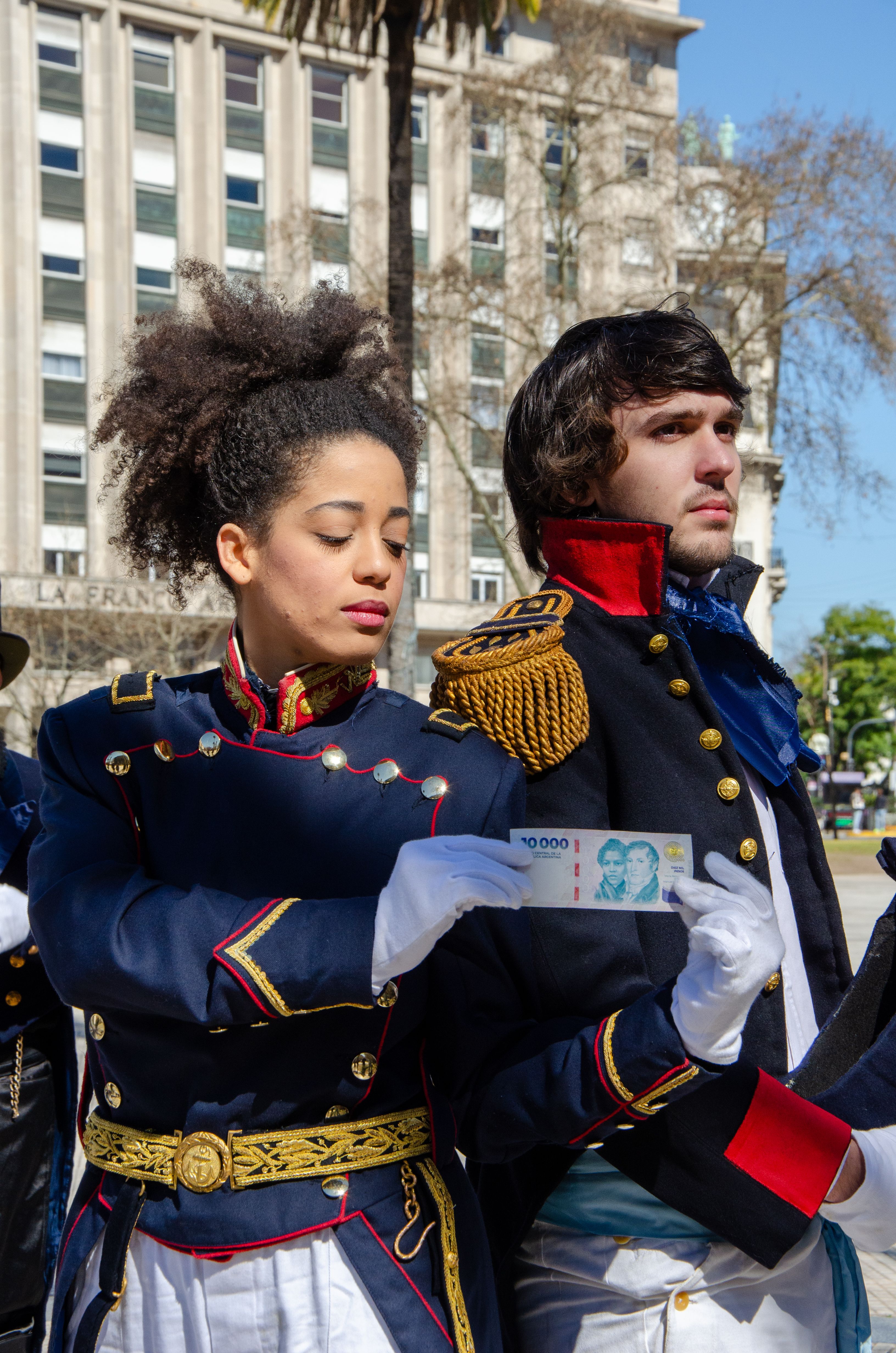 Historical reenactors in Buenos Aires wearing 19th-century military costumes, holding currency.