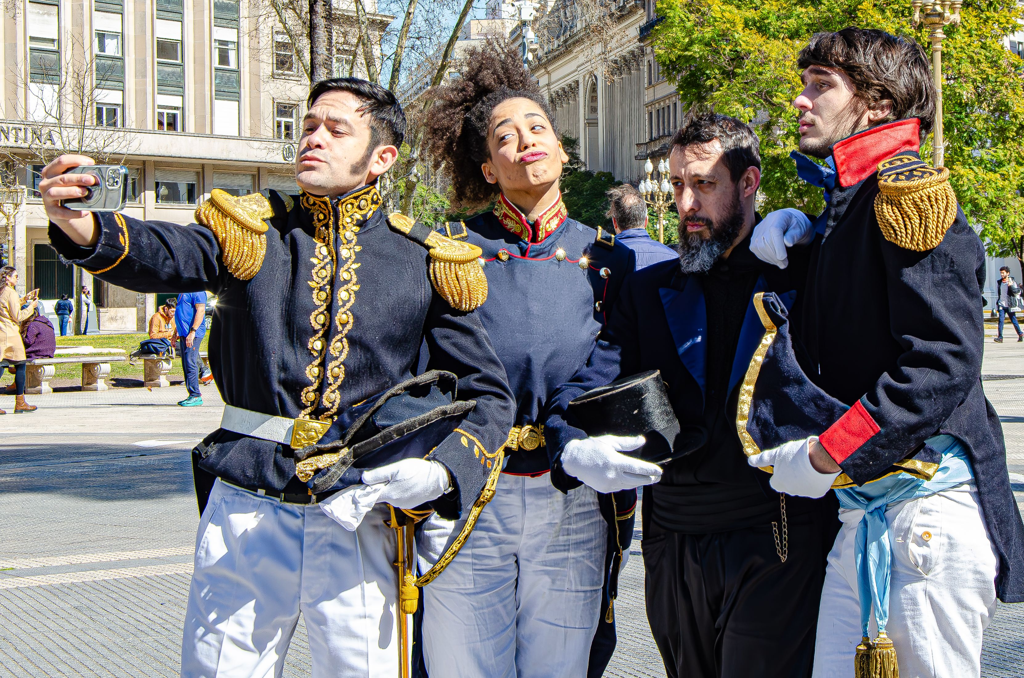 People in historical military uniforms pose for a selfie in outdoor urban setting.