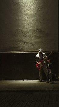 A street musician plays bass guitar under a spotlight in Puebla, Mexico, at night.