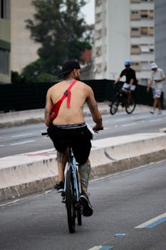 A tattooed man cycles shirtless in a city setting, showcasing urban fitness style.