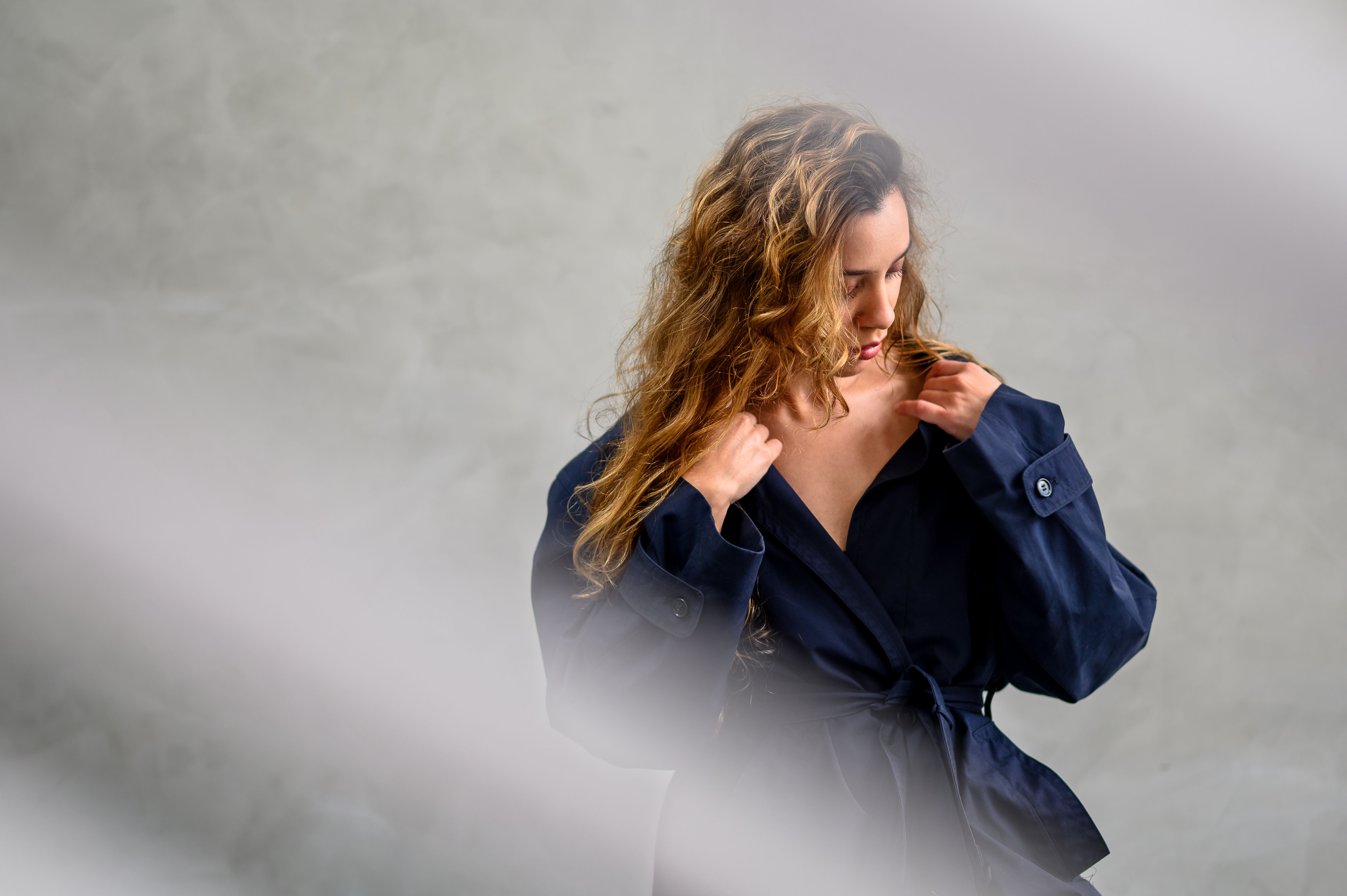 Stylish studio portrait of a woman in a blue jacket with a soft, elegant pose and blurred foreground.