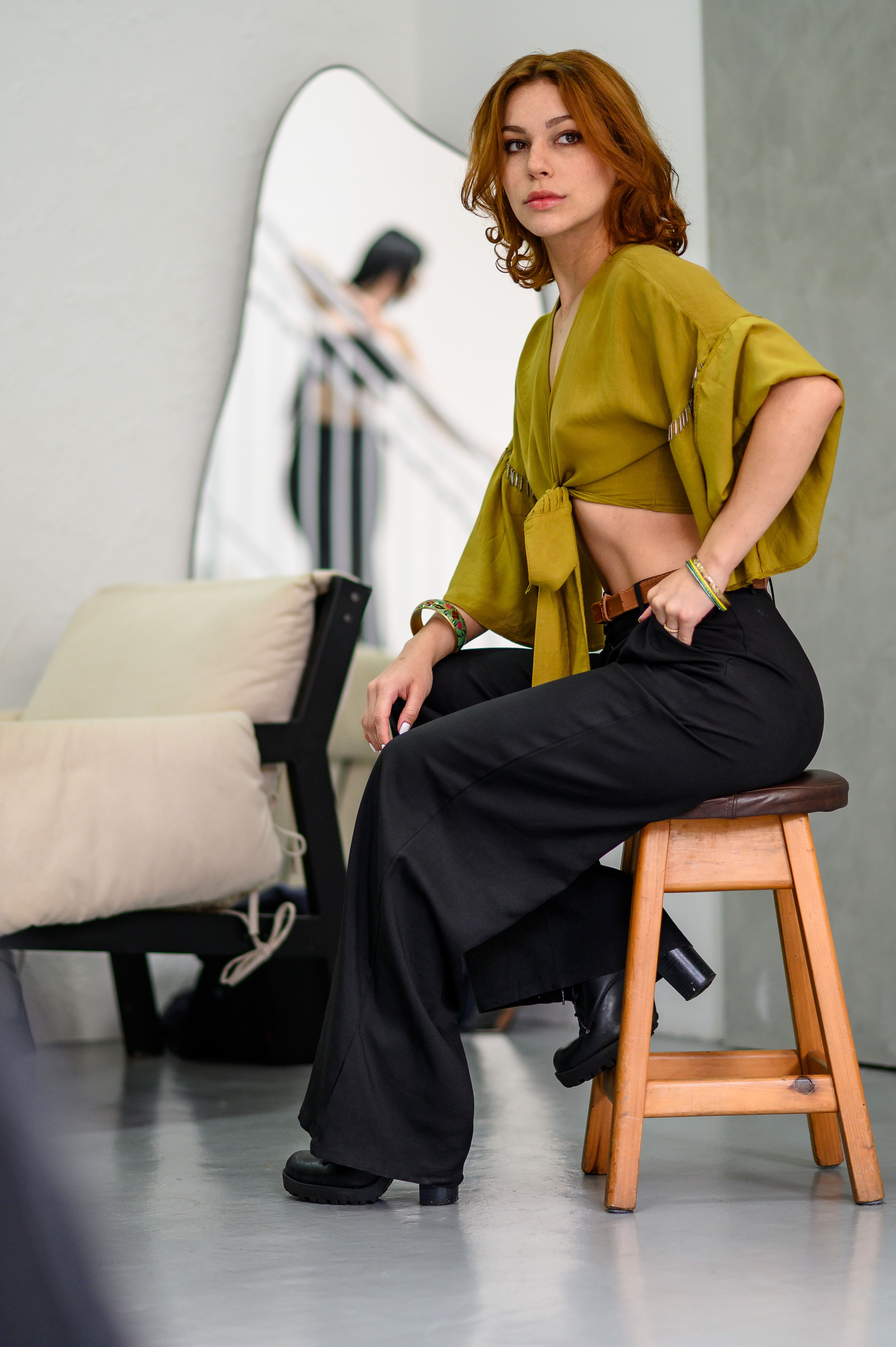 Mulher vestida na moda posa confiantemente em um banquinho em um estúdio moderno.