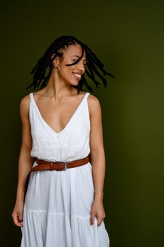 Elegant woman in white dress posing gracefully against a muted green backdrop.