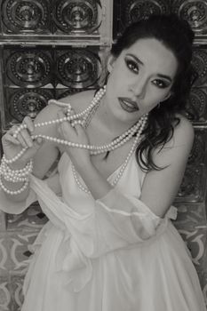 Black and white portrait of a stylish woman adorned with pearl jewelry and dramatic makeup.