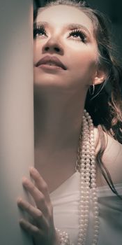 A thoughtful and elegant portrait of a young woman wearing pearls, looking upwards in soft lighting.