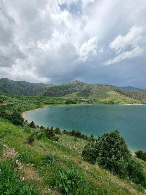 Free Peaceful mountain lake with lush greenery and dramatic clouds, perfect for nature lovers. Stock Photo