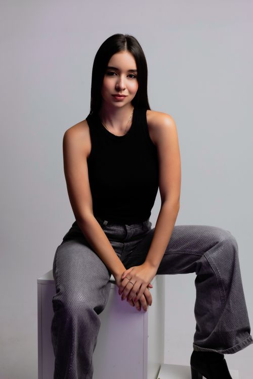 Free Stylish portrait of a young woman sitting indoors with a neutral background. Stock Photo