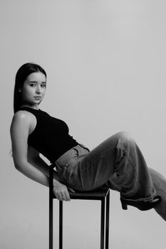 Elegant black and white portrait of a woman leaning on a chair, depicting modern fashion style.
