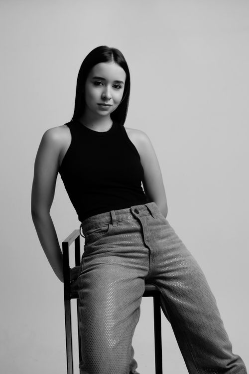 Free Black and white portrait of a young woman sitting in a minimalist setting, exuding confidence and style. Stock Photo