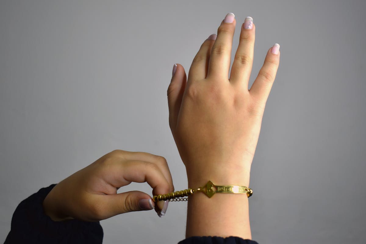 Primo piano di mani che allacciano e regolano un bracciale d'oro lucido
