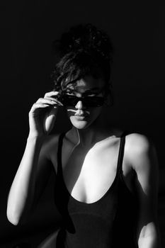 Artistic black and white portrait of a woman adjusting sunglasses in dramatic lighting.