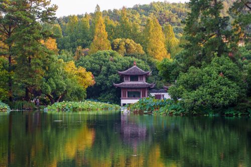 Free A traditional Chinese pavilion surrounded by lush greenery overlooking a calm lake. Stock Photo