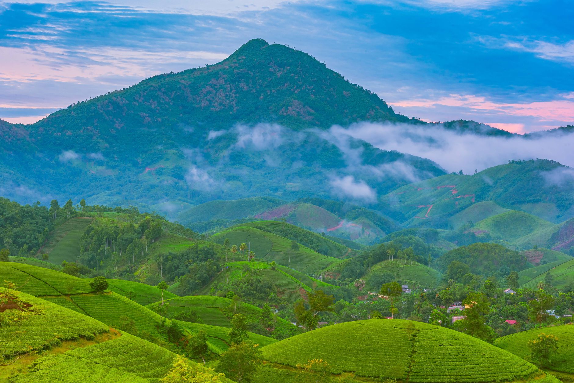 Breathtaking view of lush green hills and misty mountains under a vibrant sky.