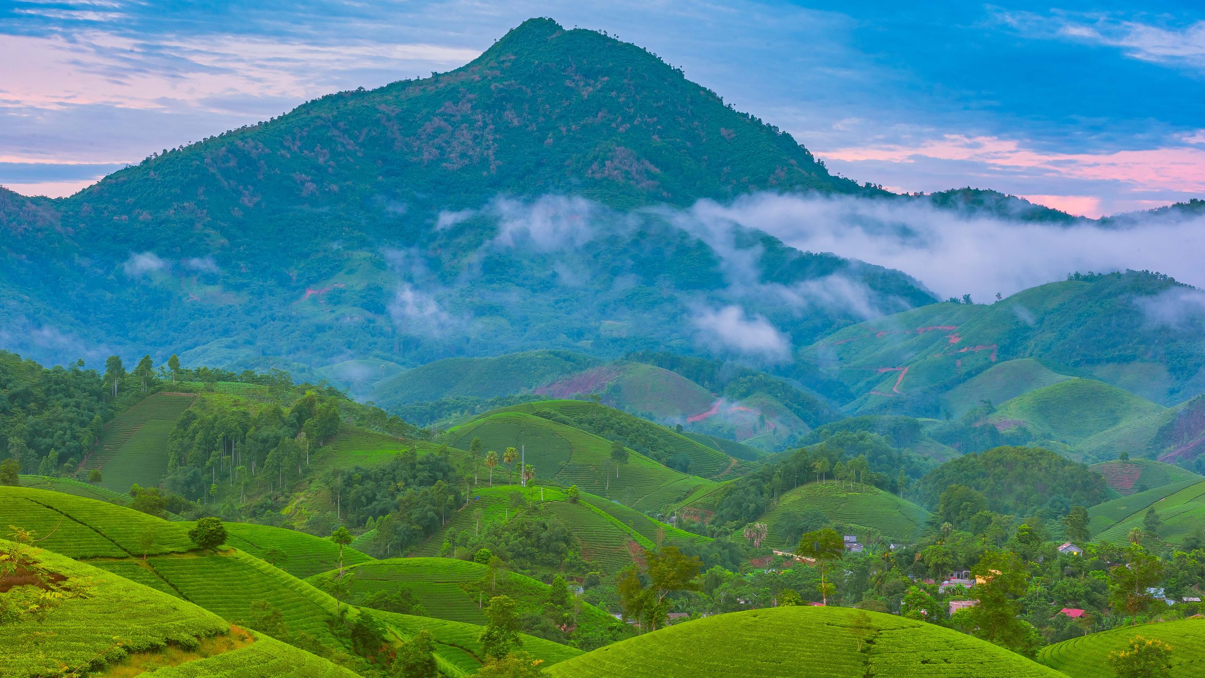 Breathtaking view of lush green hills and misty mountains under a vibrant sky.