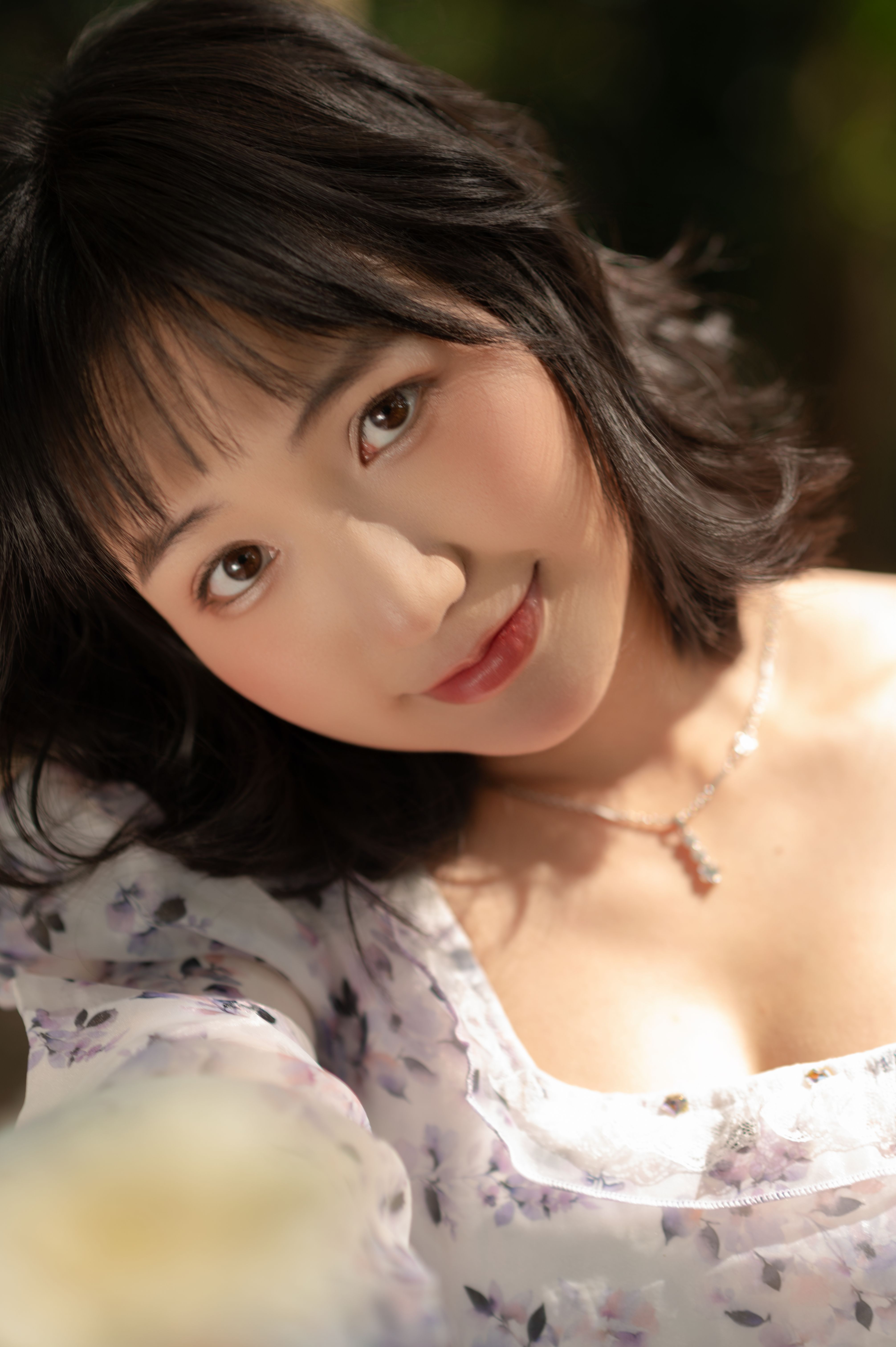 Charming portrait of a woman in soft lighting wearing a floral dress, smiling gently.
