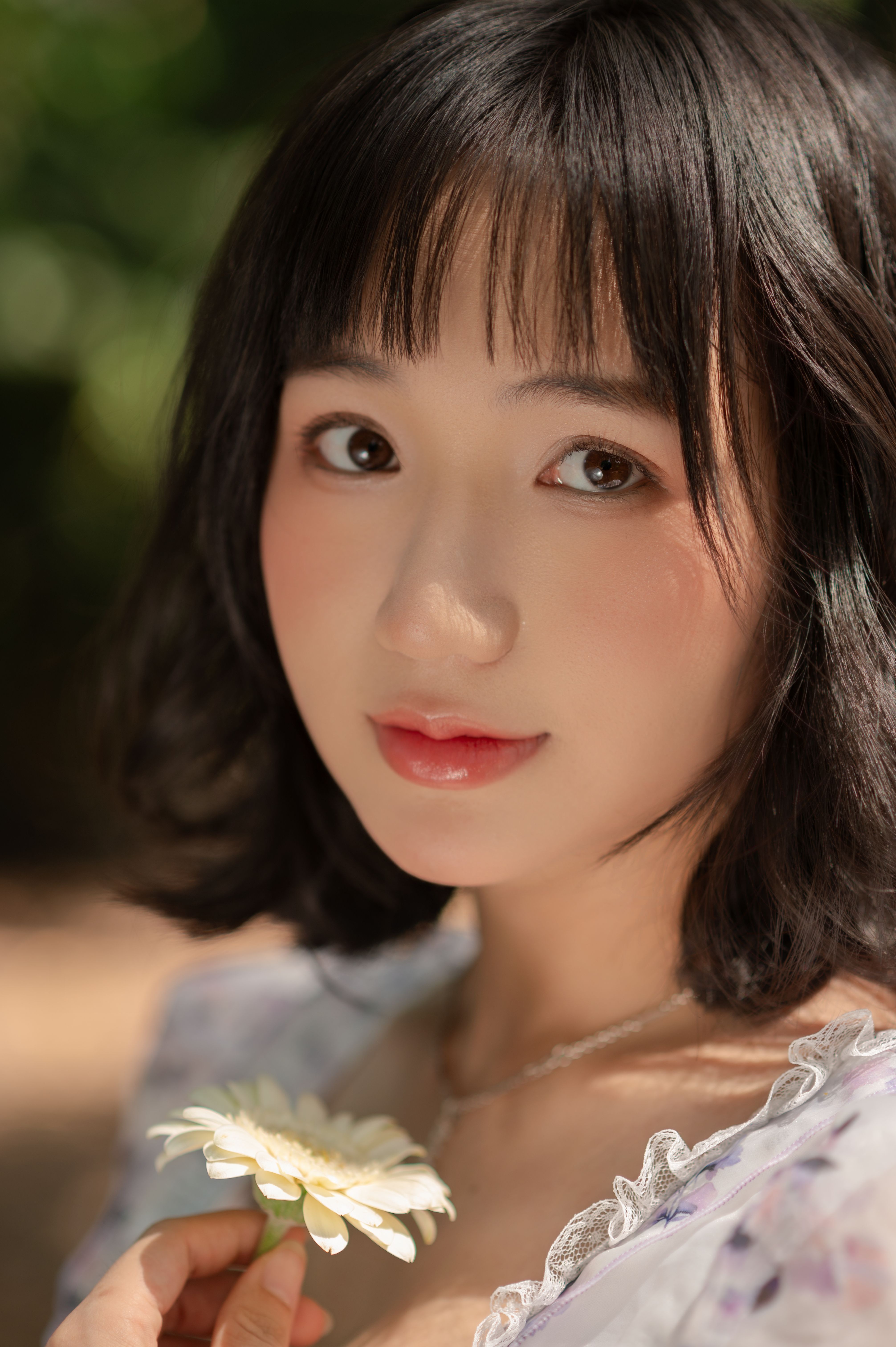 A serene portrait of a young woman holding a daisy, captured with warm natural light.