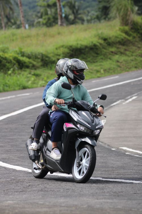 Free Two individuals on a scooter enjoying a ride on a winding road surrounded by greenery. Stock Photo