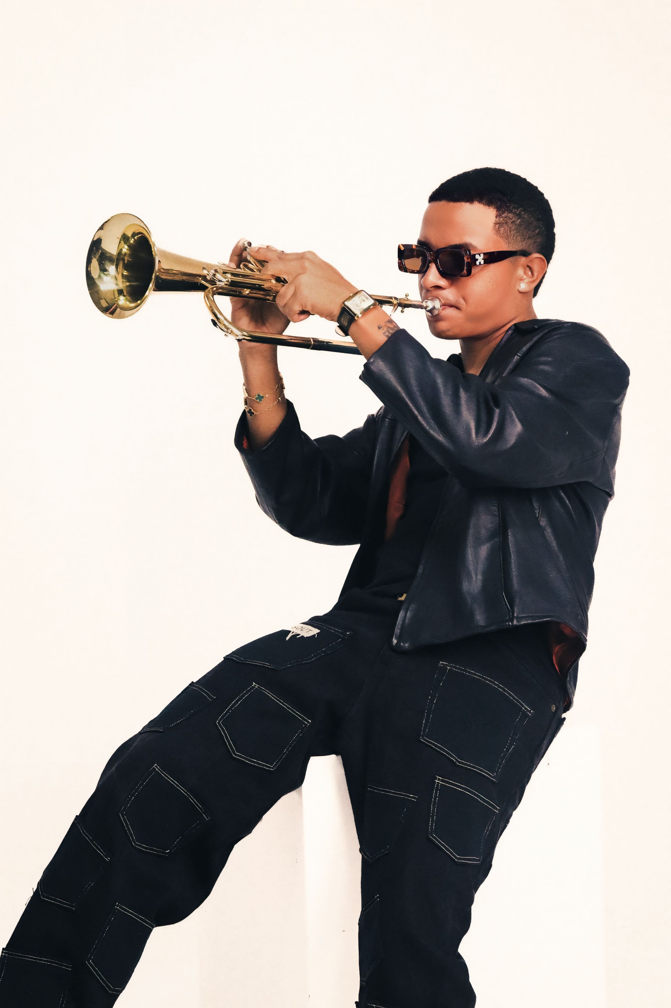 A fashionable young man wearing sunglasses plays a trumpet with a focused expression.