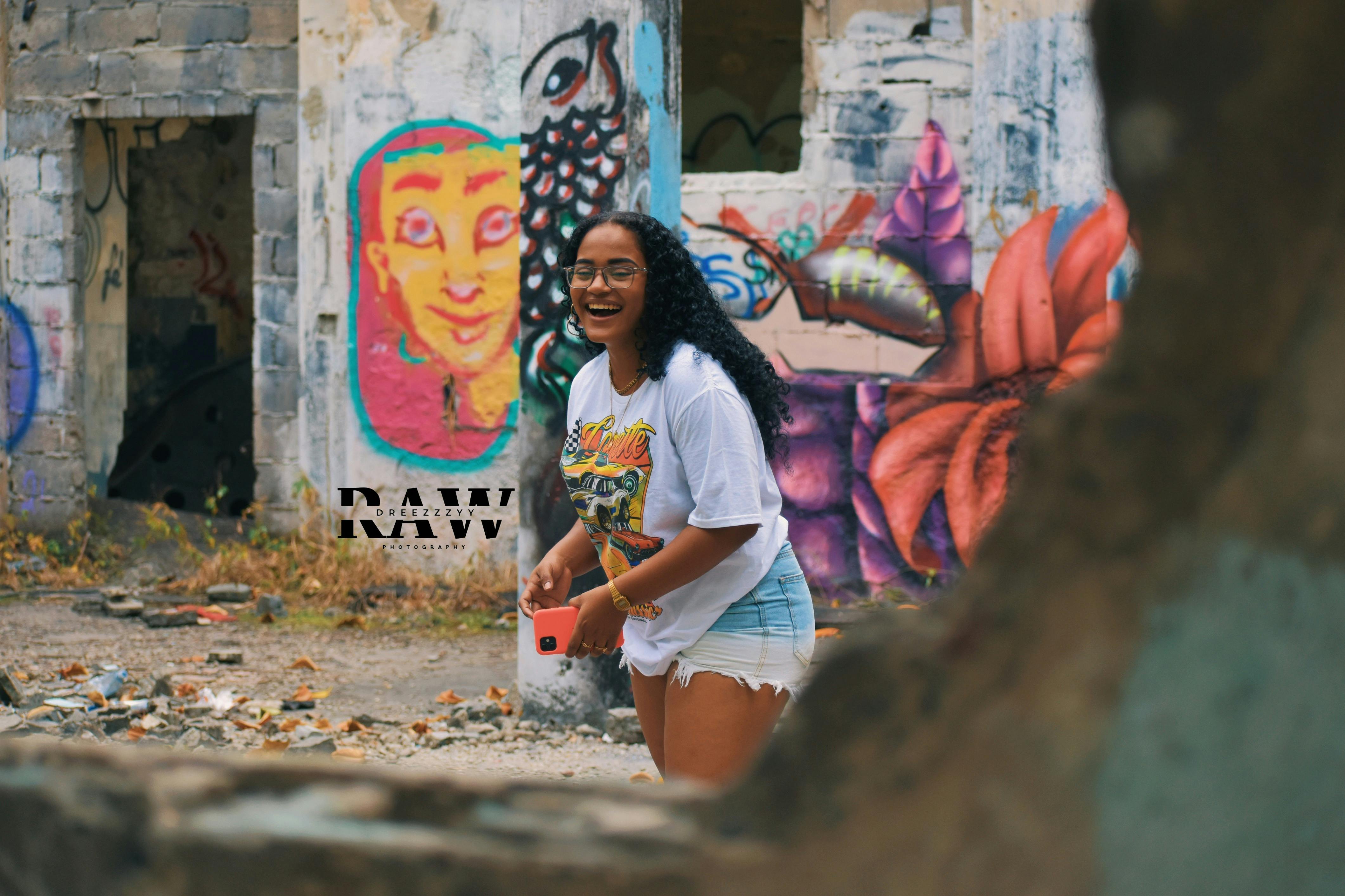 Woman enjoying urban exploration with colorful graffiti backdrop, capturing a joyful moment.