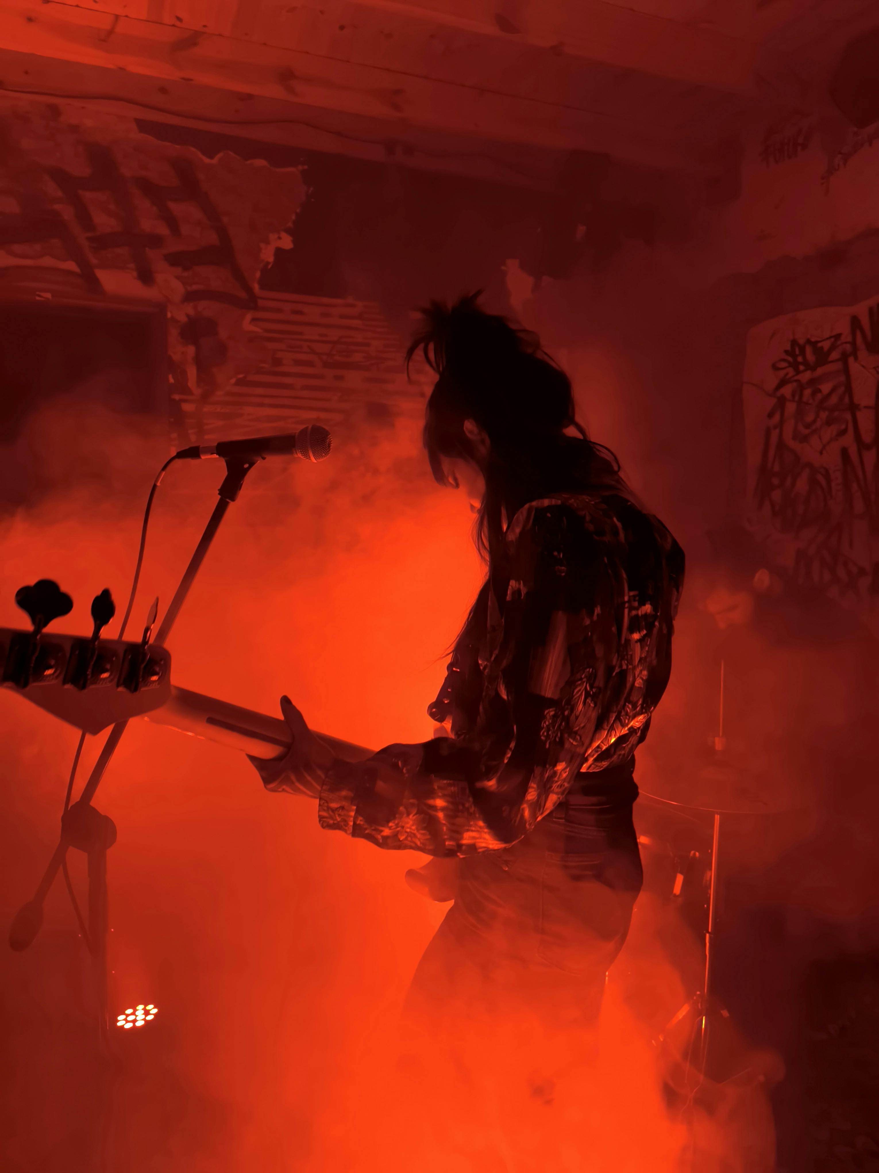 Silhouette of a musician playing guitar in a smoky, vibrant red-lit atmosphere.