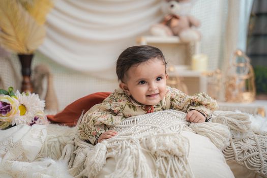 Cute baby lying on a soft decorative blanket indoors, surrounded by plush toys and cozy decor.