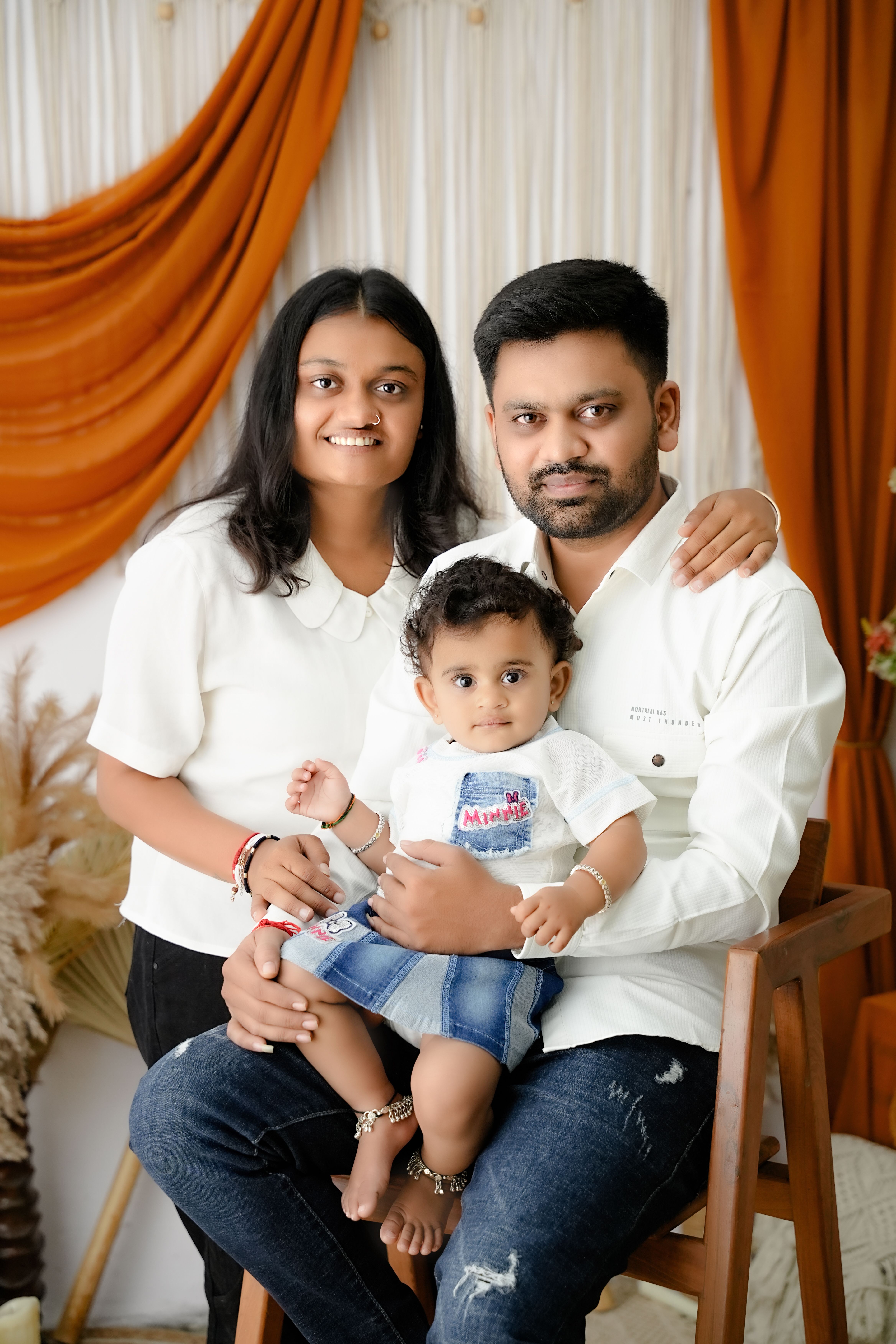 Cheerful family portrait featuring parents and baby in a cozy indoor setting.