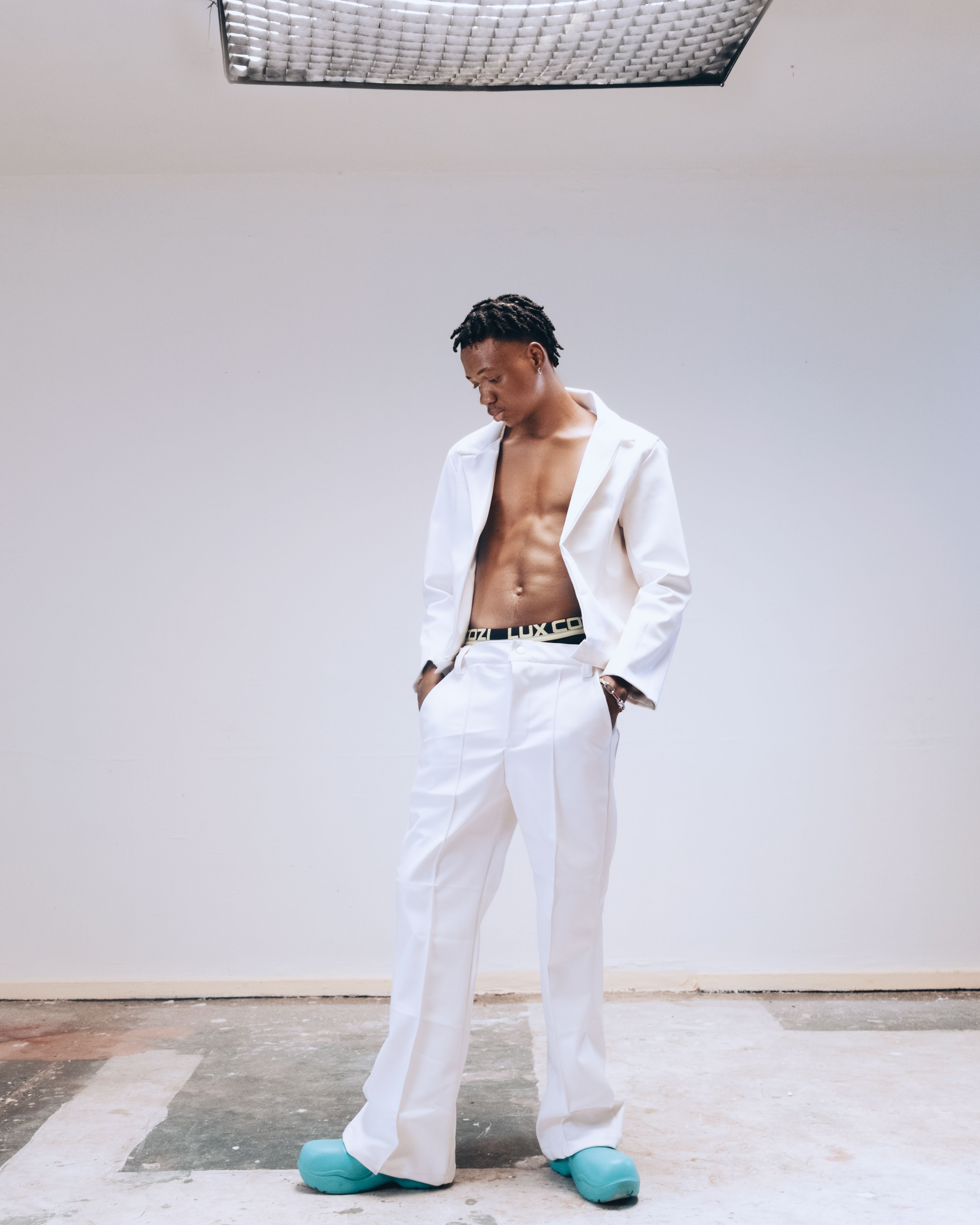 Stylish man poses indoors in chic white suit and trendy blue sneakers.