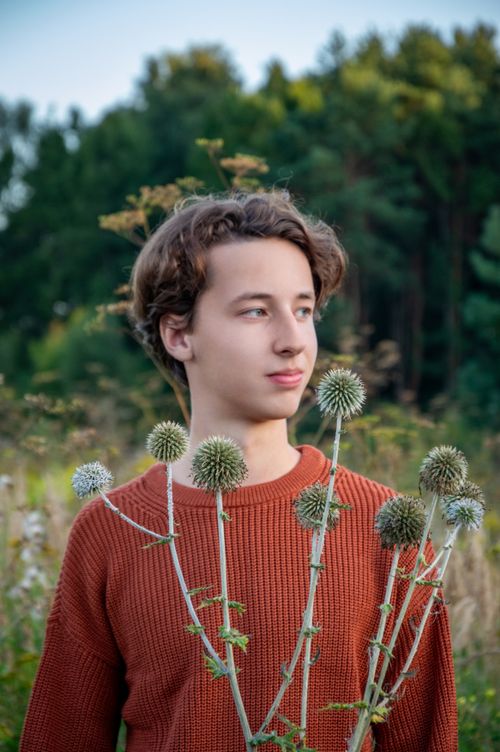 Free A young person standing in a forest with autumn flowers, wearing a rust sweater. Stock Photo