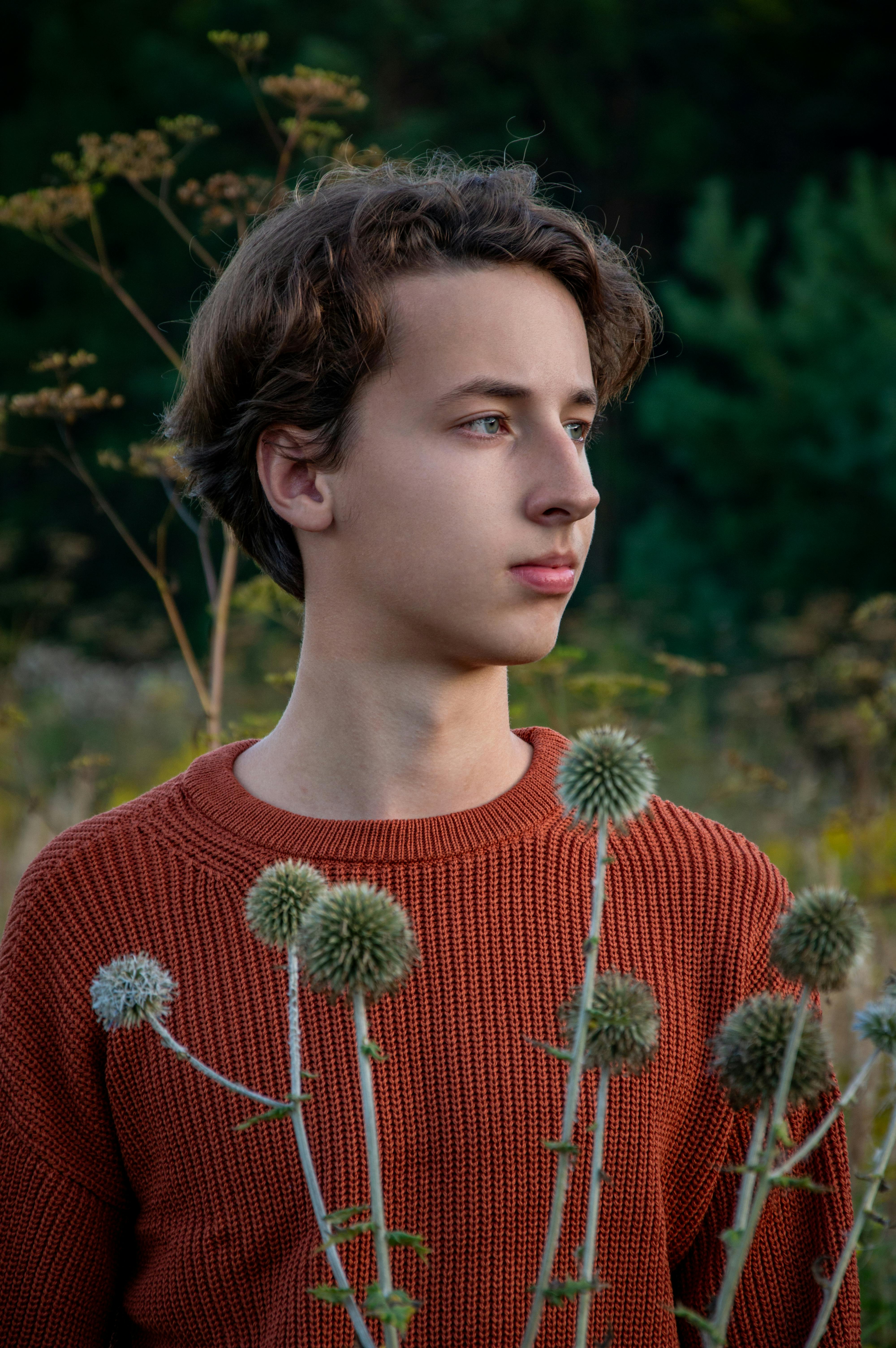 Free A young man in a rust sweater gazes contemplatively in an autumn field with wildflowers. Stock Photo