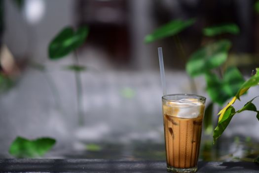 Refreshing iced coffee with straw amidst greenery in outdoor setting.