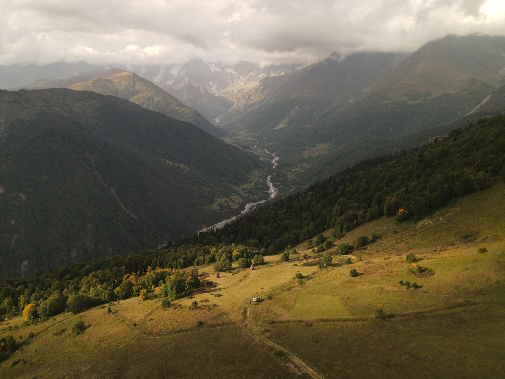 Aerial view of the picturesque Svaneti Mountains in Georgia with lush valleys and cloudy skies.