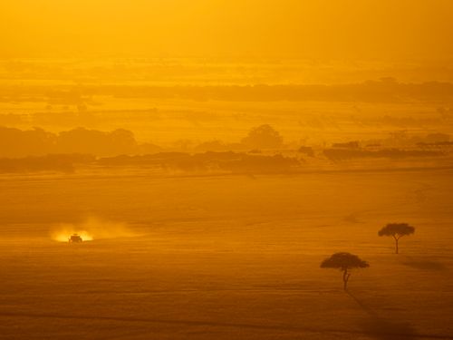 Free Dramatic view of Kenya's savanna during sunset. A vehicle drives through the golden landscape. Stock Photo