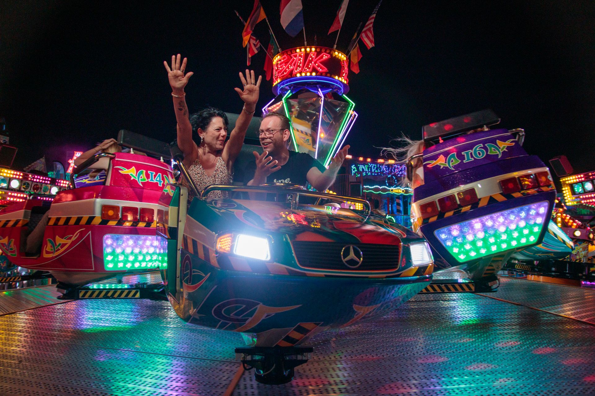Happy couple enjoying a thrilling ride at an amusement park at night.