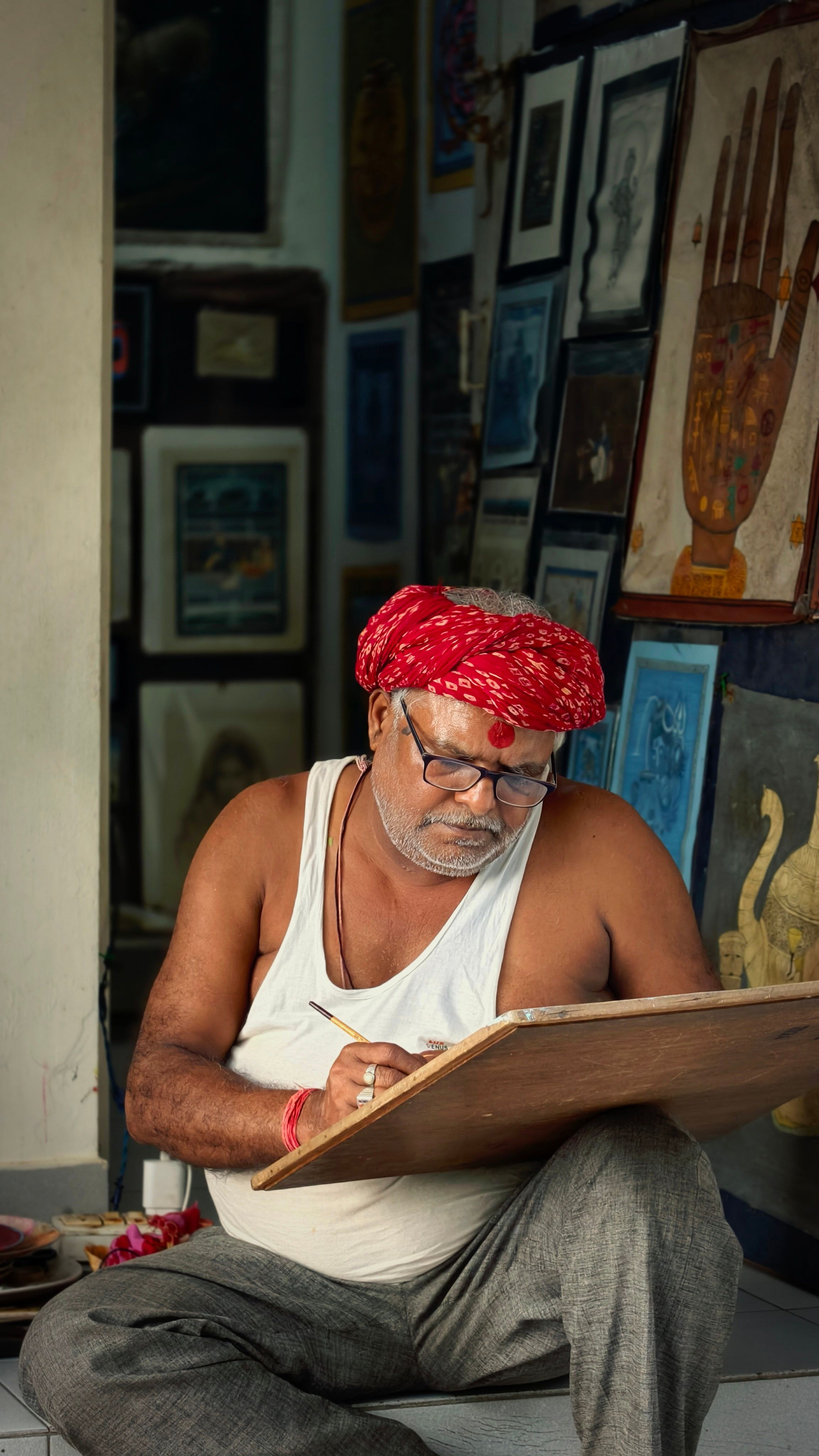 A senior artist focused on sketching in an art-filled studio with cultural artifacts.