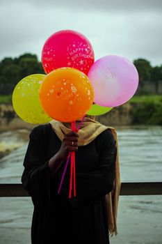 A person holding colorful 'Happy Birthday' balloons by a waterfront, creating a joyful scene.