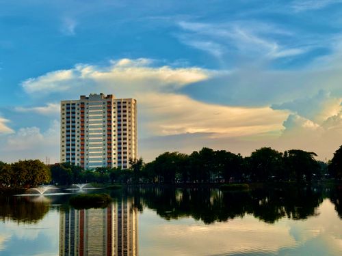 Free High-rise building reflecting in a tranquil lake with vibrant sunset sky. Stock Photo