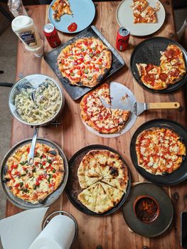 Top view of a table filled with various pizzas, pasta, and beverages, perfect for a feast.
